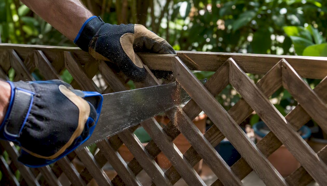 Hands cutting wood lattice panel for repair